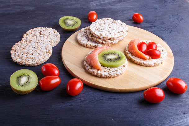 Rice cakes with salmon, kiwi and cherry tomatoes on dark  wooden background. close up. - Photo, Image