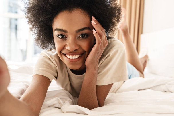 Happy young african woman taking a selfie while laying in bed - Foto, immagini