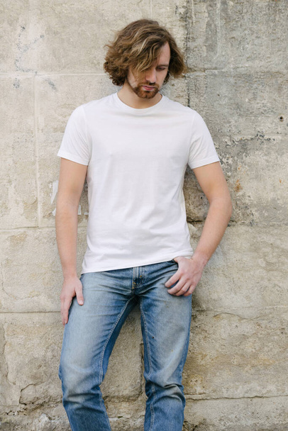 Hipster handsome male model wearing white blank t-shirt with space for your logo or design in casual urban style on europian streets - Foto, afbeelding