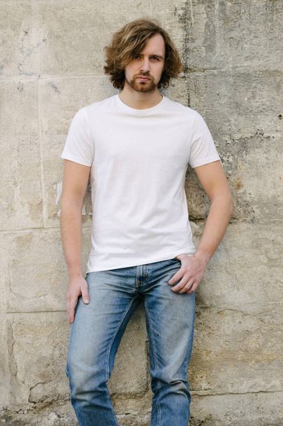 Hipster handsome male model wearing white blank t-shirt with space for your logo or design in casual urban style on europian streets - Фото, изображение