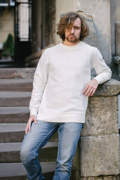 Man wearing white sweatshirt or hoodie for mock up, logo designs or design prints with with free space among europe city streets. - Foto, Imagem