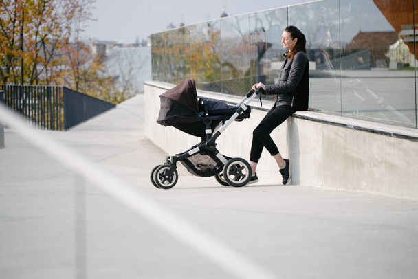 Mother with a pram or stroller on modern city streets walking and relaxing in autumn - Фото, изображение