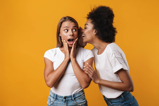 Image of emotional young multiracial girls friends gossiping isolated over yellow wall background - Foto, immagini