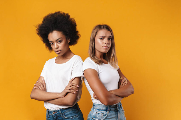 Image of displeased offended young multiracial girls friends isolated over yellow wall background - Фото, изображение
