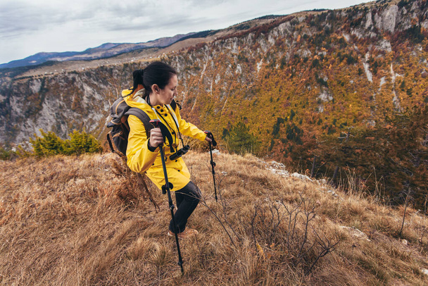 Mujer de mediana edad feliz con mochila y impermeable de pie en la cima de la montaña - Foto, Imagen