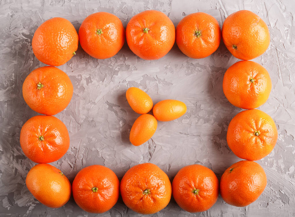 Rows of tangerines forming a rectangle and and three kumquats inside on a gray concrete background, top view, flat lay. - Foto, Imagem