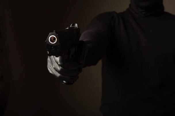 a gun in the hands of a robber on a black background - Foto, Bild