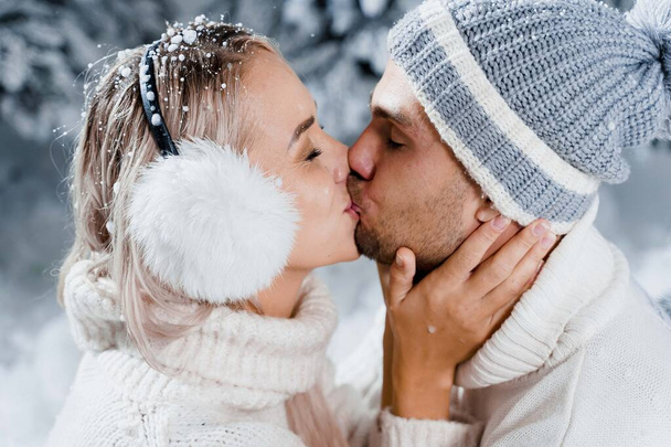 Novoroční milostný příběh. Pár polibků a objetí. Lidé nosili kožešinová sluchátka, klobouky, bílé svetry. Šťastný mladý pár objetí a polibek v blízkosti vánoční stromky v zimním dni. - Fotografie, Obrázek