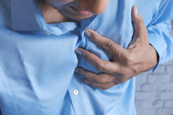 jonge man lijden pijn in het hart en houden borst met de hand  - Foto, afbeelding