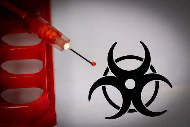 Bluttropfen auf Spritzenspitze neben Biohazard-Symbol - Foto, Bild