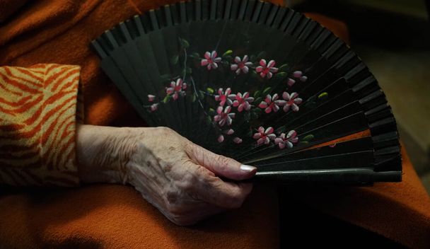 μη αναγνωρίσιμο χέρι ηλικιωμένης γυναίκας που κρατάει ανεμιστήρα χεριού - Φωτογραφία, εικόνα