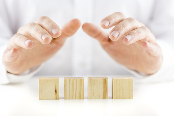 Man holding his hands protectively over a row of four blank cube - Foto, Imagen