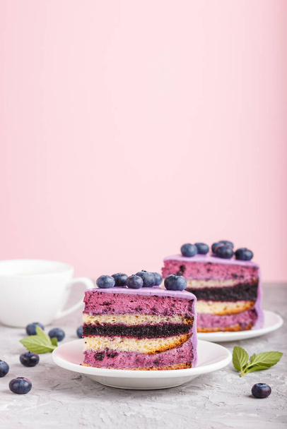 Homemade cake with souffle cream and blueberry jam with cup of coffee and fresh blueberries on gray and pink background. side view, selective focus, copy space. - Fotó, kép