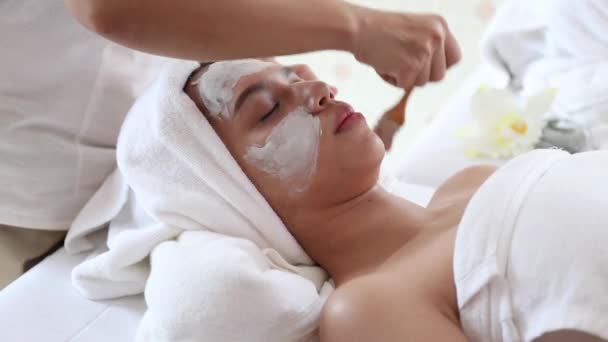 schoonheidsspecialiste gebruik spatel naar toepassing wit gezichtsmasker op jong aziatisch vrouwen wang, vdo door camera zoom in - Video