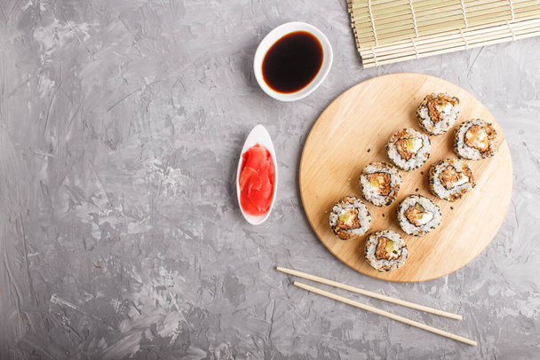 Rollos de sushi maki japoneses con salmón, sésamo, palillos de pepino, salsa de soja y jengibre marinado sobre tabla de madera sobre un fondo de hormigón gris. Vista superior, espacio para copiar, plano. - Foto, imagen
