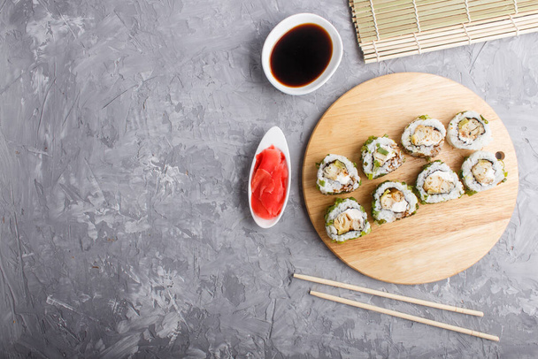 Rollos de sushi maki japoneses con cebolla verde, palillos, salsa de soja y jengibre marinado sobre tabla de madera sobre un fondo de hormigón gris. Vista superior, espacio para copiar, plano. - Foto, Imagen