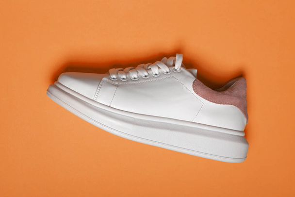 Белые кожаные кроссовки на синем и оранжевом фоне. Пара модных белых спортивных туфель или кроссовок с копировальным местом. Плоская постель - Фото, изображение