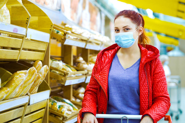 Young woman in mask posing in supermarket near bread shelves - 写真・画像