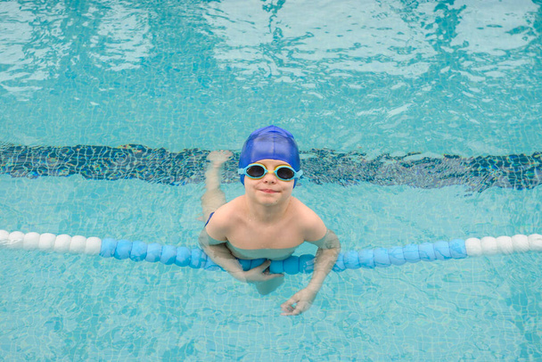 Вид сверху 7-летнего мальчика, играющего и плавающего в бассейне, улыбающегося и смеющегося - Фото, изображение