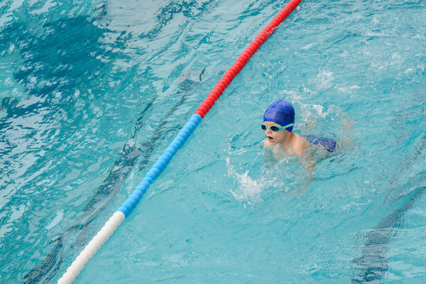top view egy 7 éves fiú játszik és úszik a medencében - Fotó, kép