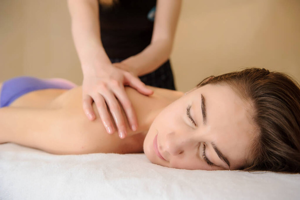vista laterale di una giovane donna che fa un massaggio sulla schiena nel salone spa - Foto, immagini