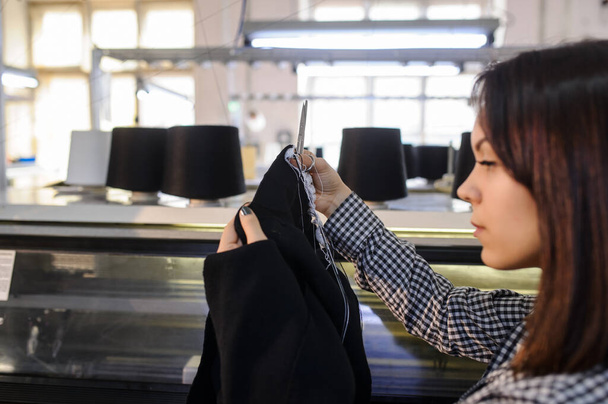 vista laterale di una giovane donna che analizza un pezzo di stoffa lavorato a maglia vicino alla macchina per maglieria industriale con coni neri su di esso - Foto, immagini