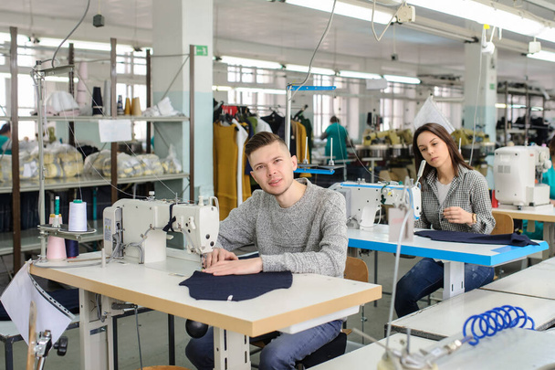 close up photo of a young man and other seamstresses sewing with sewing machine in a factory - Zdjęcie, obraz