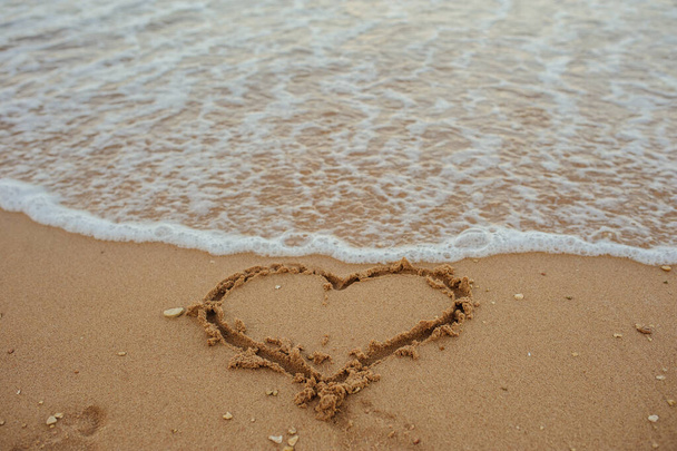 close up foto de um coração desenhado na areia de uma praia com onda e luz solar - Foto, Imagem