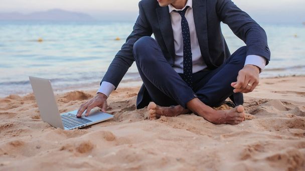 zbliżenie zdjęcie młodego człowieka w garniturze z laptopem pracującego na plaży i rozmawiającego z kimś - Zdjęcie, obraz