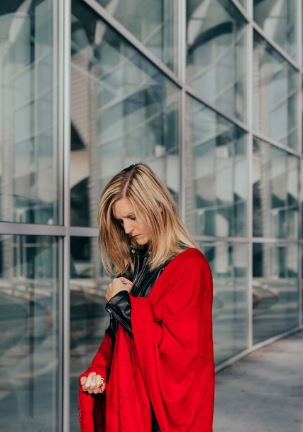 Портрет привлекательной молодой кавказской блондинки, завернутой в красный шарф с бизнес-зданием - Фото, изображение