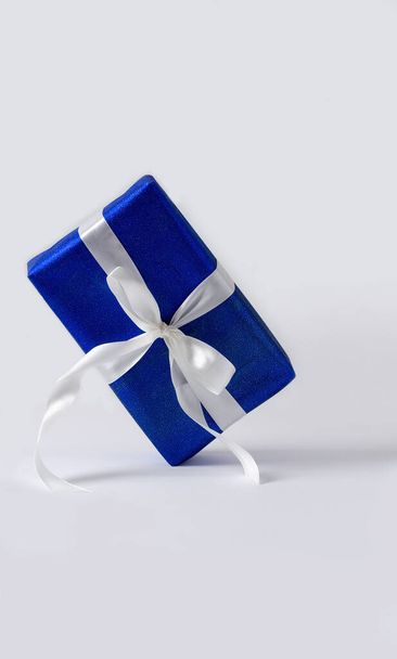 Подарочная коробка из голубой бумаги с белой лентой на белом фоне. Подарочная концепция на Новый год, Рождество, День Святого Валентина, поздравления с копией космического вертикального изображения - Фото, изображение