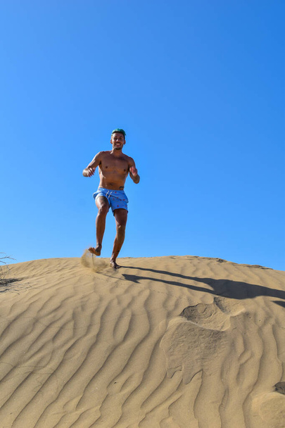 Hombre de vacaciones, corriendo y saltando en las dunas de arena del desierto. - Foto, Imagen