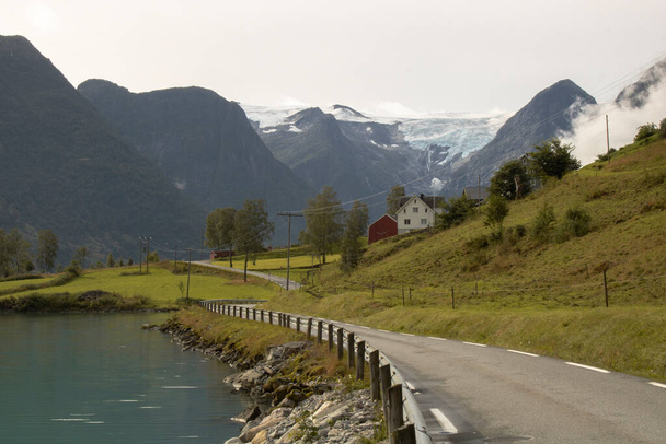 Пейзаж, изображающий дорогу рядом с домом и снежными горами на заднем плане в Норвегии - Фото, изображение