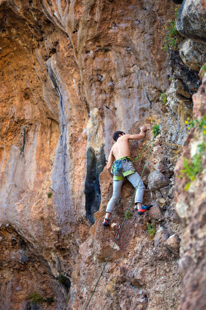 Un hombre fuerte sube a un acantilado. El escalador supera una difícil ruta de escalada en un terreno natural. Escalada en roca en Turquía. Hermosa roca naranja. - Foto, Imagen
