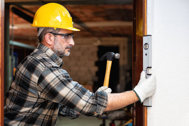 Ácsmunkás a munkahelyen csavarhúzóval, megjavítja és beszereli a szoba ajtókeretét. Építőipar. Ácsmunka. - Fotó, kép