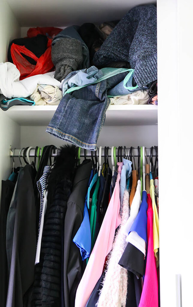 Garderobe mit verschiedenen Kleidungsstücken. Kleine Raumfahrtorganisation. Der Kontrast von Ordnung und Unordnung. Vertikale Lagerung - Foto, Bild