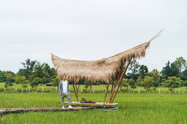 Чоловік сидить біля бамбукового мосту на рисовому полі
 - Фото, зображення