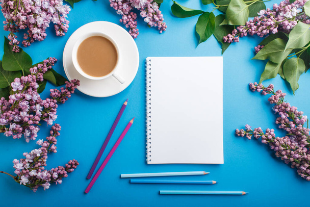 Purple lilac flowers and a cup of coffee with notebook and colored pencils on pastel blue background. Morninig, spring, fashion composition. Flat lay, top view. - Fotoğraf, Görsel