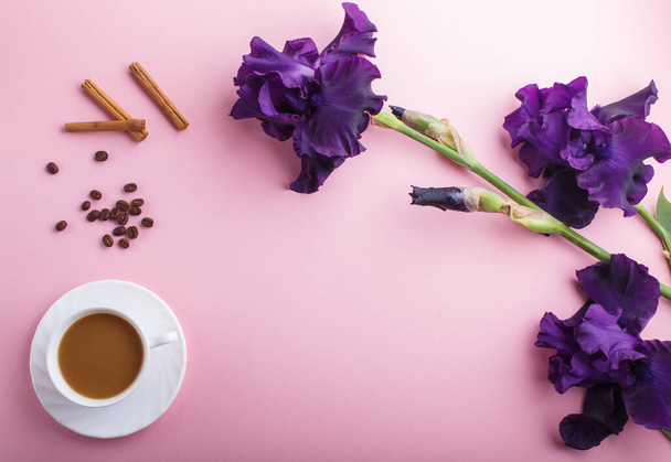 Фиолетовые цветы ириса и чашка кофе на розовом фоне. Доброе утро, весна, модная композиция. Плоская кладка, вид сверху, копировальное пространство. - Фото, изображение
