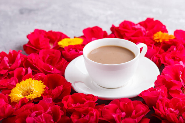Fleurs roses rouges et une tasse de café sur un fond de béton gris. Morninig, printemps, composition de mode. vue latérale, mise au point sélective, gros plan. - Photo, image