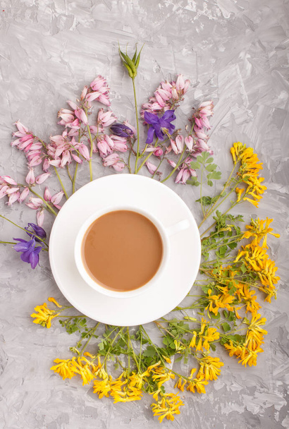 Yellow, pink and blue flowers in a spiral and a cup of coffee on a gray concrete background. Morninig, spring, fashion composition. Flat lay, top view, close up. - Foto, Imagen
