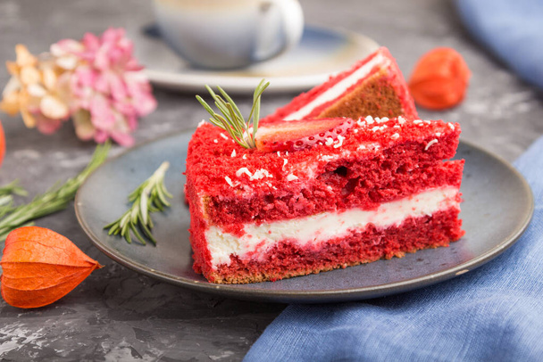 Σπιτικό κόκκινο βελούδινο κέικ με κρέμα γάλακτος και φράουλα με φλιτζάνι καφέ σε μαύρο μπετόν φόντο με μπλε ύφασμα. πλαϊνή όψη, κοντινό πλάνο, επιλεκτική εστίαση. - Φωτογραφία, εικόνα