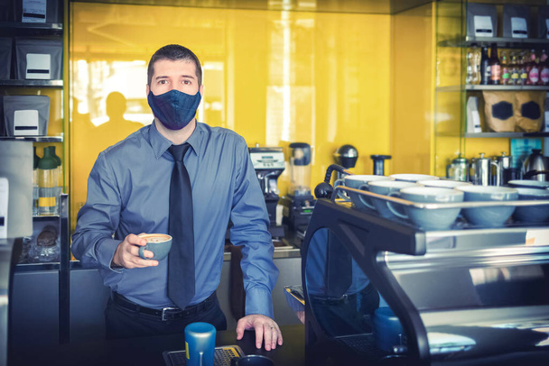 Felice piccolo imprenditore con maschera protettiva che serve caffè dietro il bancone dopo la riapertura del negozio - Foto, immagini