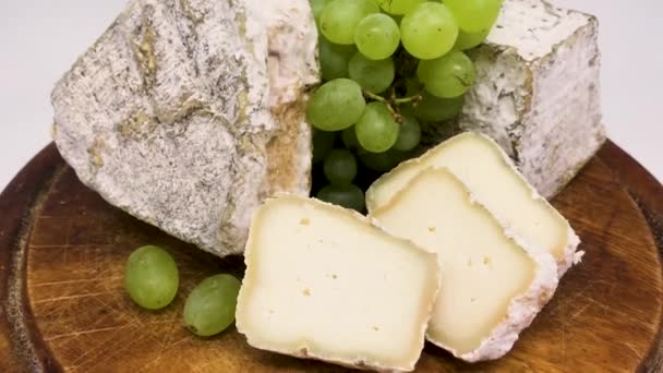  Um prato de queijo de leite de cabra bolorento variado em uma tábua de madeira com uvas verdes - Filmagem, Vídeo