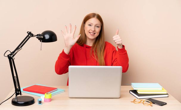 Jeune étudiante dans un lieu de travail avec un ordinateur portable comptant six avec des doigts - Photo, image