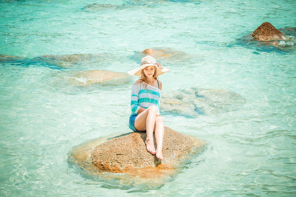 Mulher relaxante em uma pedra no oceano azul
 - Foto, Imagem