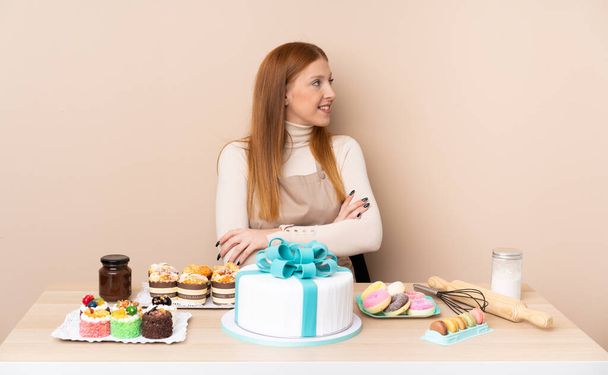 Молода руда жінка з великим тортом дивиться в бік
 - Фото, зображення