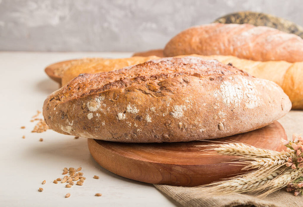 Różne rodzaje świeżego pieczonego chleba na białym drewnianym tle. widok z boku, zbliżenie, ostrość selektywna. - Zdjęcie, obraz