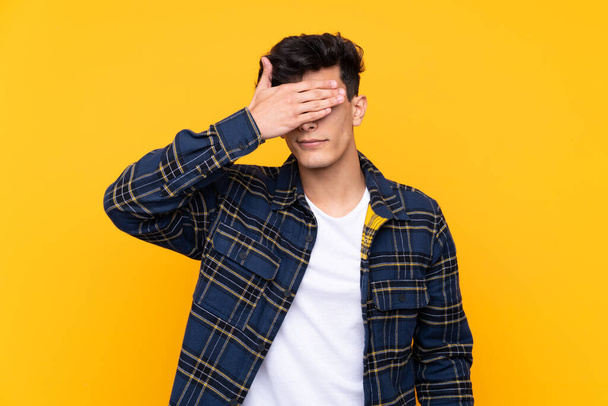 Young Argentinian man over isolated yellow background covering eyes by hands - Фото, зображення