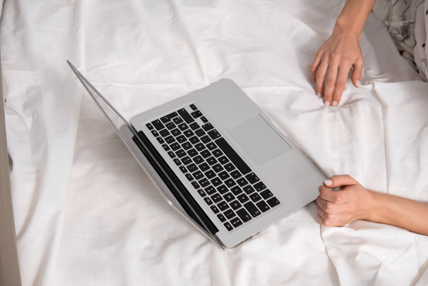 Top view of a woman sitting on a bed , using laptop. Working at home concept. Girl is working on her laptop in bed with white linens. Relaxing working process. Stay at home. - Fotografie, Obrázek